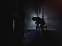 Eine Silhouette einer Person befindet sich in einem dunklen Raum und wird durch ein Licht leicht angestrahlt.