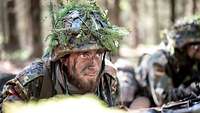 Ein Soldat mit getarntem Gesicht und Helm im Wald.