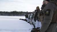 Soldaten stehen in einer Reihe aufgestellt im Schnee. Im Hintergrund ist ein Wald.