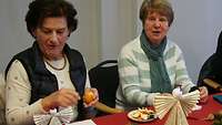 Zwei Frauen essen eine Mandarine nach dem Basteln von Papierengeln.