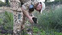 Ein Soldat in Uniform stellt an einem Stab eine Fotokamera auf.