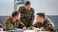 Zwei Soldaten sitzen an einem Tisch, daneben steht eine Soldatin, die mit ihnen spricht.
