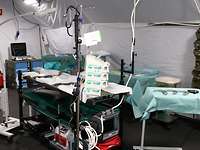 There are stretchers, medical equipment and instruments inside a large tent.