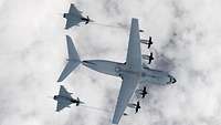 Ein Transportflugzeug vom Typ A400M 54+16 betankt zwei Kampfjets vom Typ Eurofighter über Wolken.