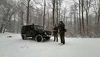 Zwei Soldaten stehen vor einem Bundeswehrfahrzeug im Schnee. Einer von ihnen blickt durch ein Fernglas.
