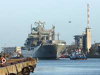 A small blue-and-white boat pulling a large gray ship on the water.