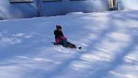 Ein Kind fährt auf einem Schlitten im Schnee.