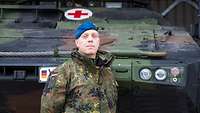 Porträt eines Soldaten mit blauem Barett vor einem Bundeswehrfahrzeug mit rotem Kreuz