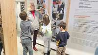 Kinder stehen mit einer Frau vor einer Informationswand.