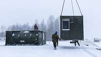 Soldaten/innen im Schnee stellen einen Container auf.