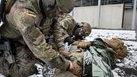 Soldaten behandeln einen simulierten Verwundeten, der vor einer Halle im Schnee liegt.