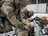 Soldaten behandeln einen simulierten Verwundeten, der vor einer Halle im Schnee liegt.