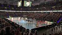 Zwei Handballmannschaften stehen in einer Arena auf dem Spielfeld. 