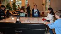 Mehrere Kinder stehen an einer Airhockey-Tafel und spielen damit. 