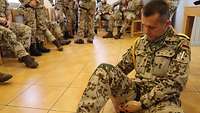 Ein Soldat sitzt am Boden und legt sich selber einen Tourniquet, eine Art Gurt zum Stillen von starken Blutungen am Bein an.