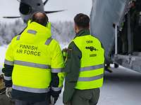 Zwei Männer in gelber Weste stehen auf Landebahn in Winter neben Ladeluke eines Militärflugzeuges