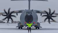 Militärischer Einweiser in gelber Weste steht vor Militärflugzeug auf schneebedecktem Flughafen