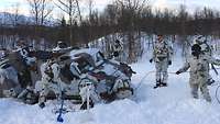 Ein Kettenfahrzeug steckt tief im Schnee fest. Soldaten stehen und hocken drum herum.