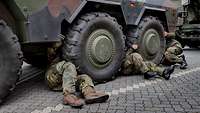 Soldaten liegen zwischen den Reifen unter einem Fahrzeug und kontrollieren es