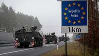 Gefechtsfahrzeuge fahren auf einer Autobahn. Rechts ein blaues Schild, darauf steht: Polen 1 km.