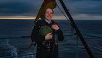 Eine lächelnde Soldatin steht am Heck eines Schiffes, hinter ihr weht die Bundesflagge im Wind