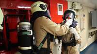 Zwei Personen im Bordgefechtsanzug mit Atemschutzgerät auf dem Rücken überprüfen Ausrüstungssitz