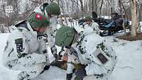 Mehrere Soldatinnen und Soldaten tragen in einer winterlichen Landschaft ein Übungspuppe 