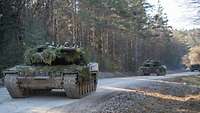 Drei Panzer fahren auf eine Schotterstraße an einem Wald vorbei