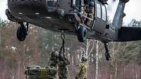 Drei Soldaten stehen unter einem Hubschrauber und hängen ein Seil an