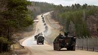 Zahlreiche Militärfahrzeuge fahren auf einer langen, staubigen Straße einen Berg hoch