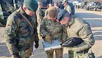 Drei Soldaten in unterschiedlicher Flecktarnuniform schauen auf eine Landkarte