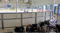 Rollstühle vor der Bande eines Eishockeyfeldes. Wehrdienstbeschädigte spielen Eishockey.