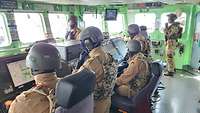 Mehrere Soldaten mit Weste und Helm auf der Brücke eines Schiffes