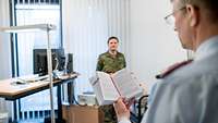 Ein Soldat steht vor einem Soldaten und ließt aus dem Buch "Disziplinarrecht der Bundeswehr"