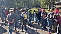 Mehrere Menschen stehen an einem Platz und beobachten das Gelände. 