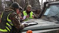 Soldat bespricht sich mit zwei anderen, vor ihnen Notizen auf der Motorhaube eines Geländefahrzeugs