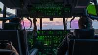 Zwei Piloten von hinten im Cockpit einer C-130J bei rötlichem Wolkenhimmel