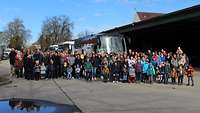 Eine größere Personengruppe steht vor drei Bussen, die sie nach München bringen.