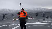 Ein Militärrabbiner in Marineuniform an Deck eines Schiffes vor schneebedeckter Landschaft.