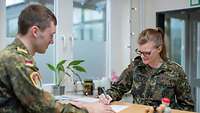 Eine Frau und ein Mann in grüner Uniform stehen sich an einem Tresen gegenüber