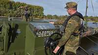 Ein Soldat steuert ein Boot hinter dem Fahrerstand. Ein weiterer Soldat steht mit dem Rücken zu ihm