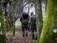 Zwei Soldaten bauen eine Kabelverbindung ab. Ein Mann trägt eine große Kabeltrommel auf dem Rücken.