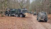 Ein Tanklastzug steht neben mehreren Militärgeländewagen in einem Wald