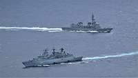Zwei graue Kriegsschiffe in See; eines fährt nach links, das andere nach rechts.