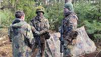 Ein Zivilist spricht mit zwei getarnten Soldaten im Wald, dahinter steht ein Zwei-Mann-Zelt.