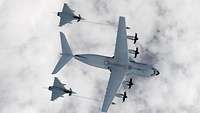 An A400M 54+16 transport aircraft refuels two Eurofighter jet fighters above the clouds.