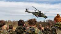 Ein Mann in Uniform sitzt an einem Tisch und registriert die wartenden Personen.