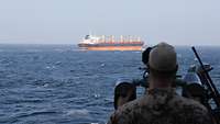 Ein Soldat beobachtet ein Handelsschiff auf offener See durch ein Fernglas