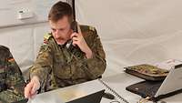 Ein Soldat zeigt mit einem Stift auf einen Computerbildschirm, während er telefoniert