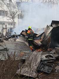 Zwei Feuerwehrleute stehen zwischen Trümmern und löschen ein Feuer